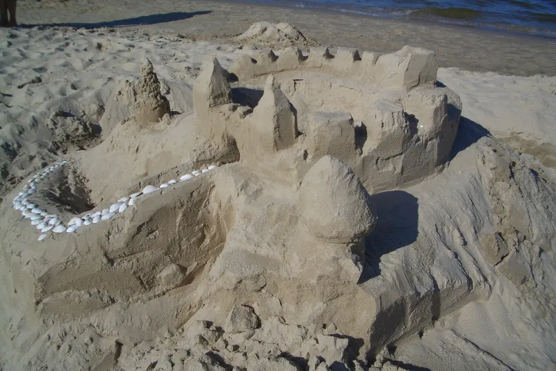 A sandcastle with towers and walls and a path lined with shells, built on a beach
