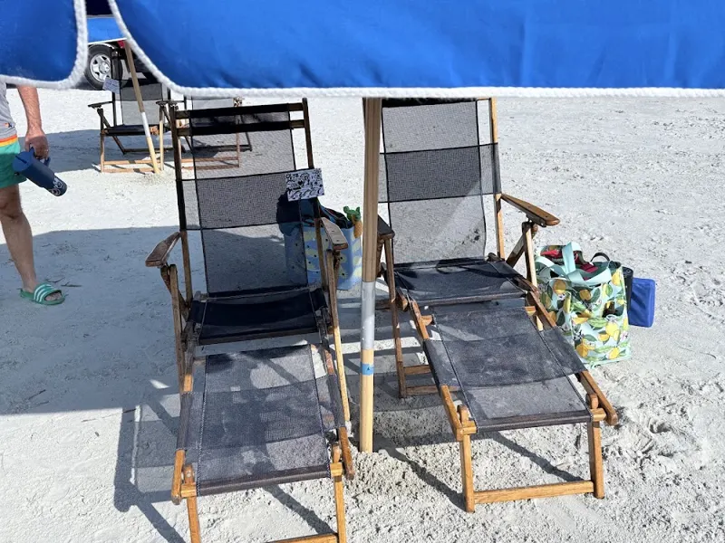 Two wooden beach chairs under a blue umbrella on white sand
