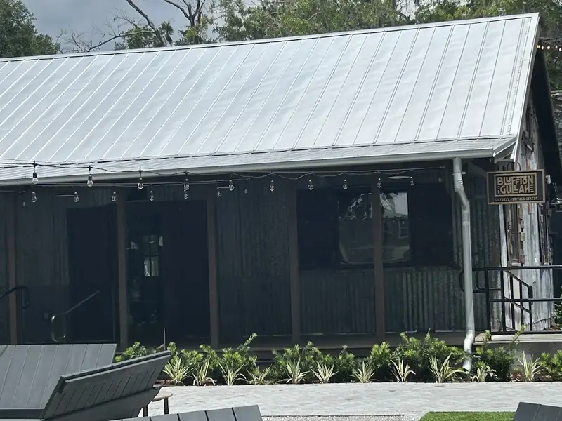 The dark board-and-batten building of the Bluffton Gullah Cultural Heritage Center, with a metal roof and its sign by the door