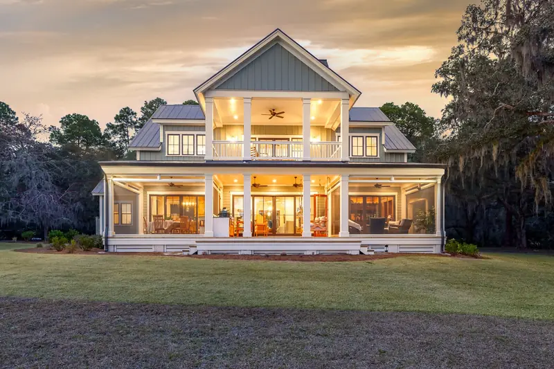 A two-story house with deep lit porches on both floors at sunset