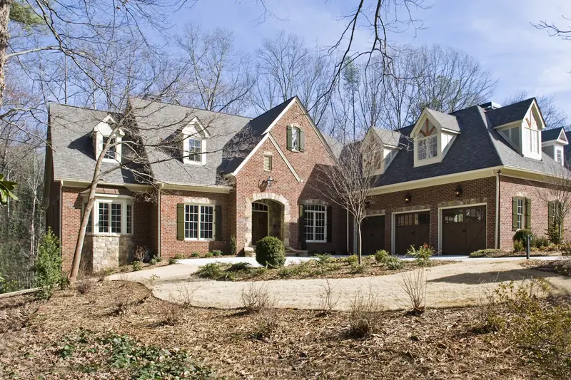 A brick house with dormers and a stone entry behind a circular drive