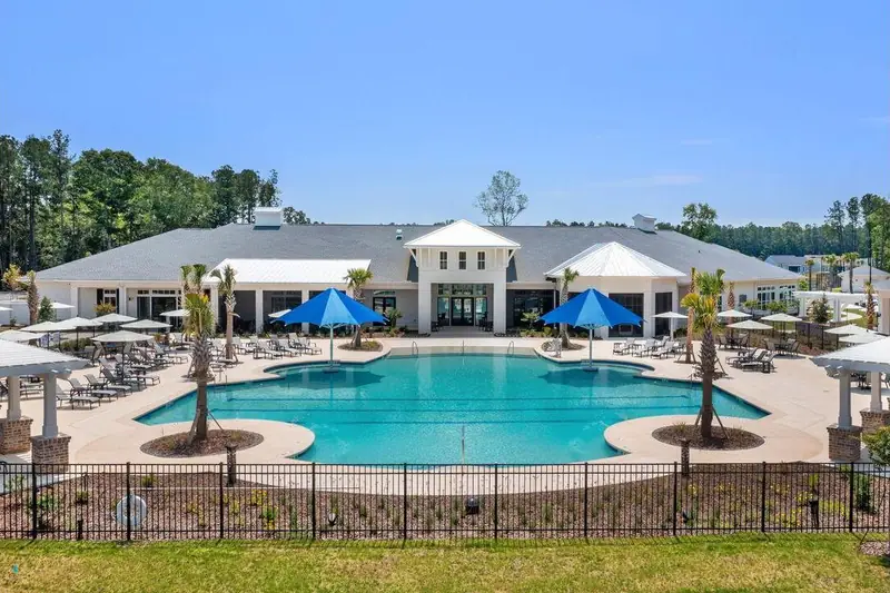 A resort-style pool with blue umbrellas in front of a white clubhouse