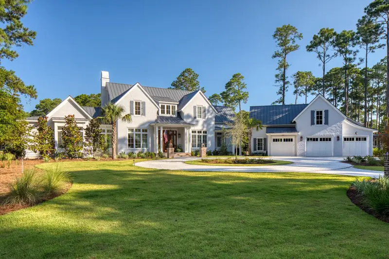 A large white house with a three-car garage across a wide lawn under pines
