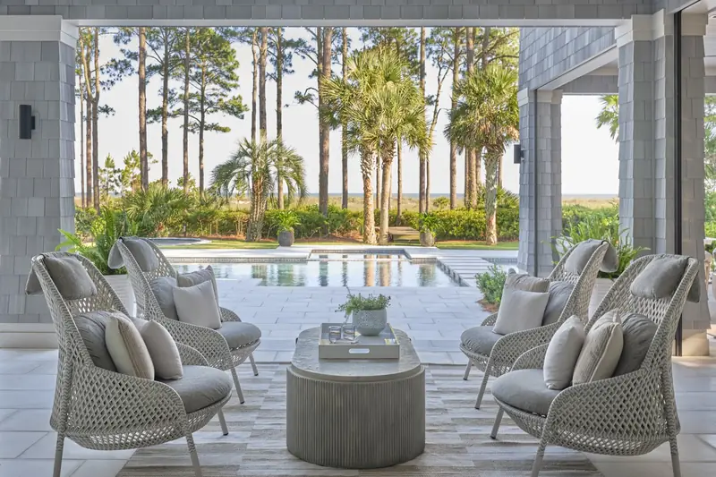 A covered porch with wicker chairs looking out over a pool to the marsh