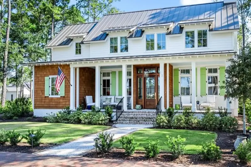 A white house with a metal roof, green shutters and a porch with an American flag