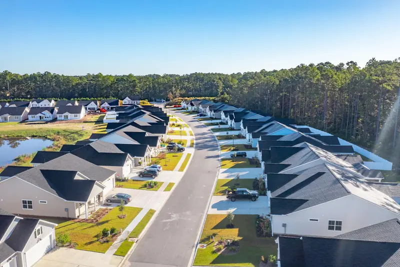 Aerial view of rows of new houses along a curving street beside a pond