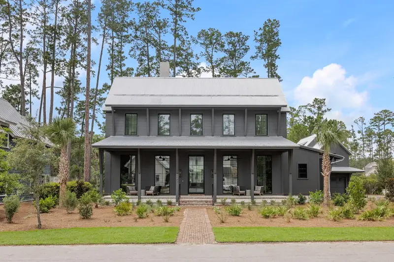 A dark-sided two-story house with a long front porch and a brick walk