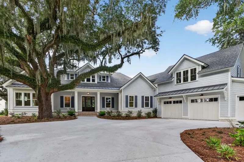 A white house with a three-car garage under a spreading live oak