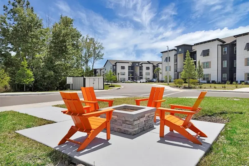 Orange chairs around a fire pit on a lawn in front of new three-story apartment buildings at Pointe Grand Southpoint in Hardeeville