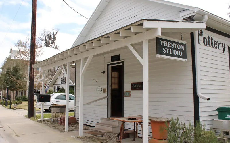 The white wooden Preston Studio building on Church Street in Old Town Bluffton, with a Pottery sign on its side and pots on the porch