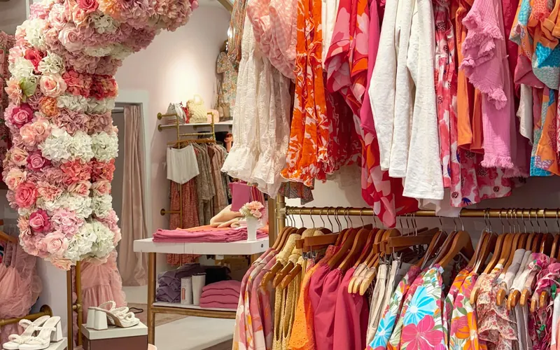 Racks of bright dresses and tops beside a floral arch inside Panache Boutique, with shoes on a small table