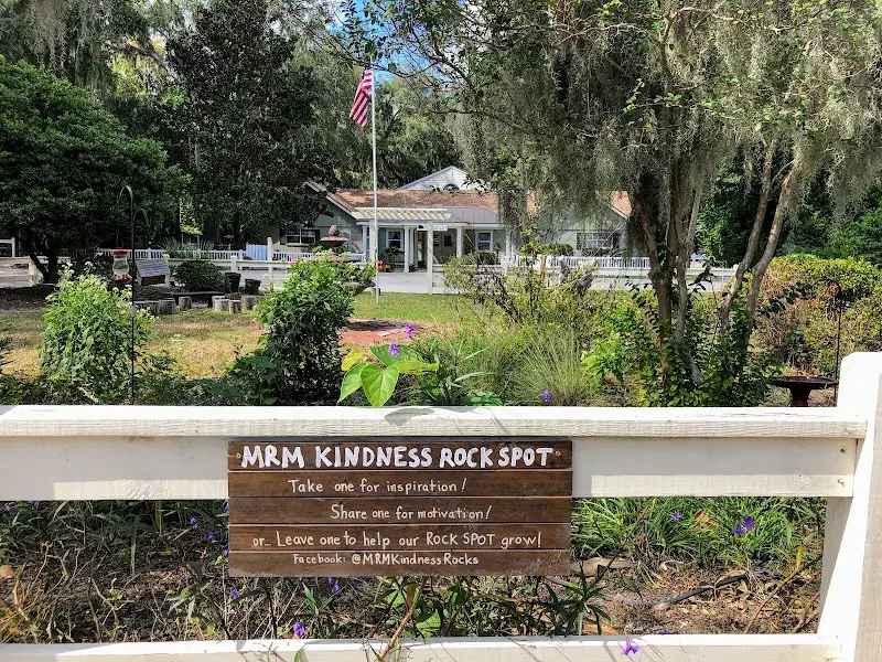 The May River Montessori campus under live oaks on Calhoun Street, with a hand-painted kindness sign on the fence