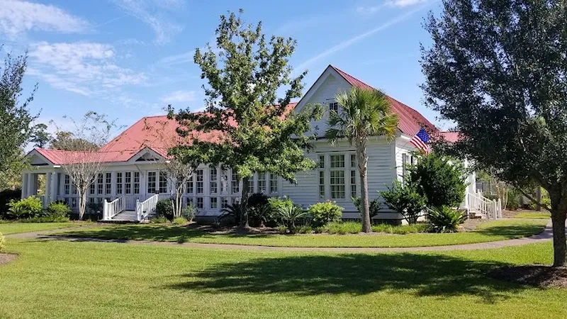 White clubhouse cottage with a red roof across a lawn under live oaks