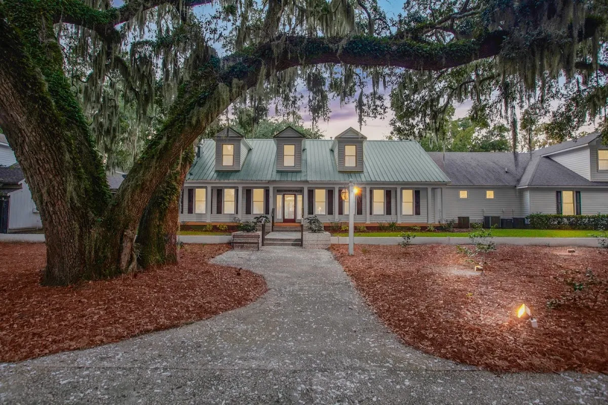 The Cat Island Club clubhouse seen past a spreading live oak hung with Spanish moss, its windows lit