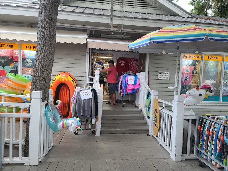 A Beach Market storefront with pool floats, inflatable rafts and beachwear on racks outside, under a striped umbrella