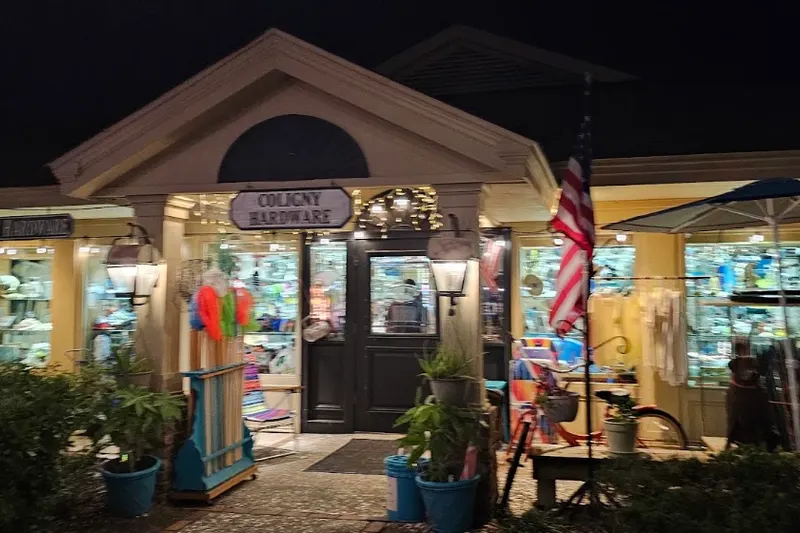The Coligny Hardware storefront at dusk, with its lit sign above the door and beach goods in the windows