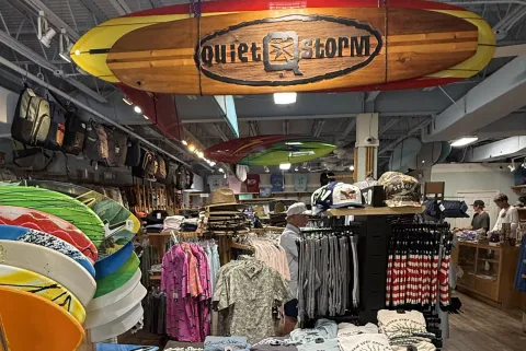 Surfboards and skimboards racked along the wall under a hanging Quiet Storm surfboard sign