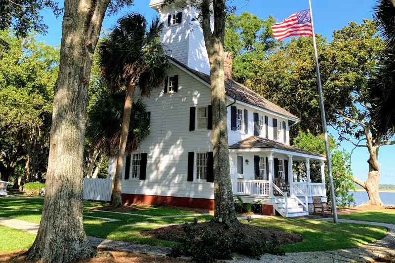 The white 1873 Haig Point Lighthouse, a house with a lantern tower, under live oaks beside Calibogue Sound
