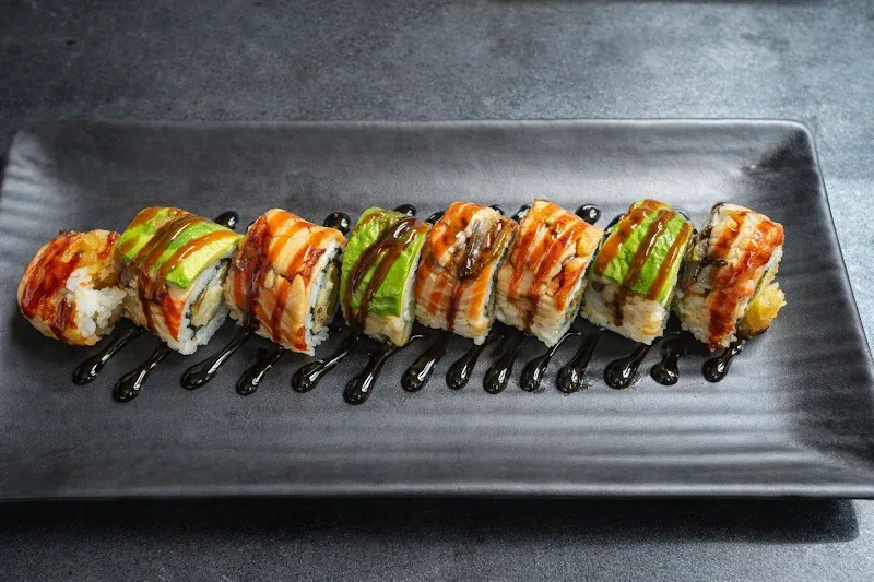 A sushi roll topped with avocado and eel sauce, sliced and served on a black plate