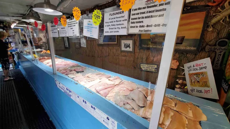 Long refrigerated counter of fresh fish fillets with handwritten price signs at Benny Hudson Seafood
