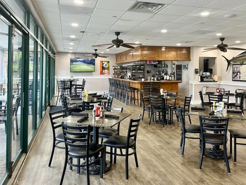 The dining room at Big Jim's BBQ with a wood bar, high-top and standard tables and a wall of windows