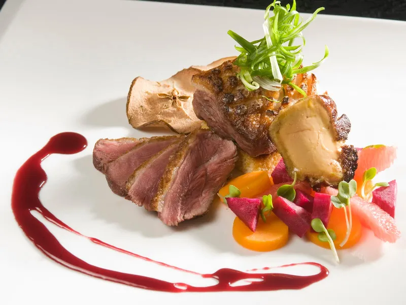 Plated duck breast with roasted vegetables and a berry sauce swoosh by Chef Aram