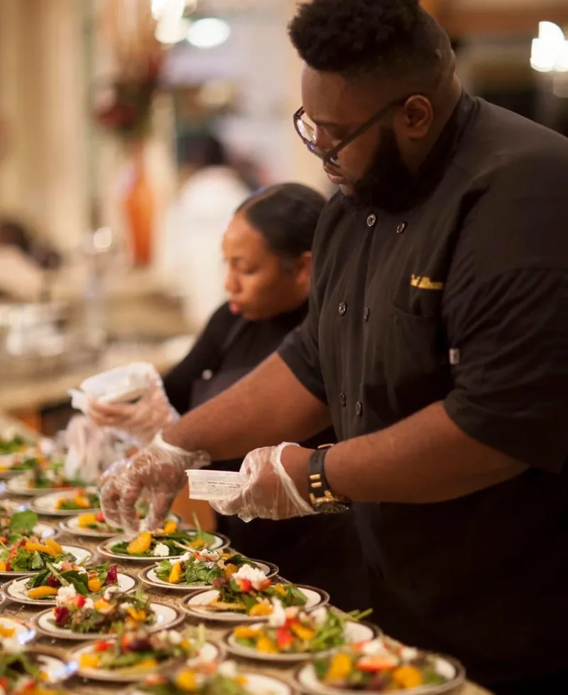 Chef Glenn Brown plating rows of salads with his team at a catered event