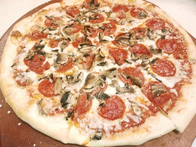 A pepperoni and mushroom pizza on a wooden board at Club Seats Grille