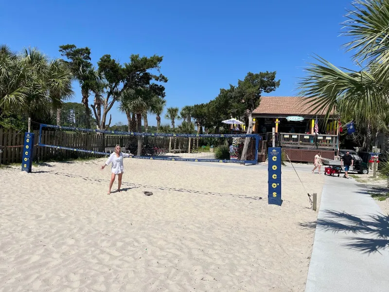 Sand volleyball court and the boardwalk beside Coco’s on the Beach, with the tiki bar’s roof in the palms behind