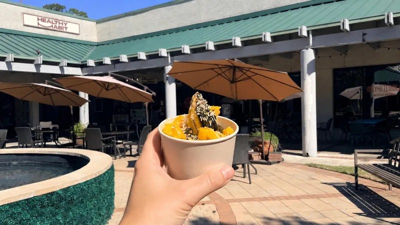 The Healthy Habit courtyard on Office Park Road with patio umbrellas, and a hand holding a bowl in front of the shop sign