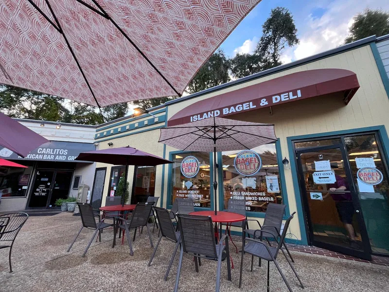 The Island Bagel & Deli storefront with its maroon awning, outdoor tables and umbrellas
