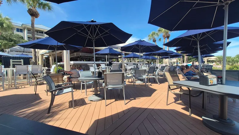The oceanfront deck at Loggerhead Landing, with navy umbrellas over grey tables and palm trees beyond