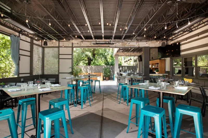 The open-air dining room at the former Lucky Rooster Kitchen + Bar, with teal metal stools and marble-topped tables
