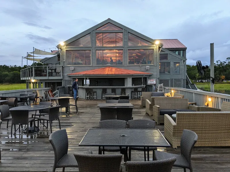 The Old Oyster Factory’s glass-fronted dining room and outdoor deck bar over the marsh at dusk