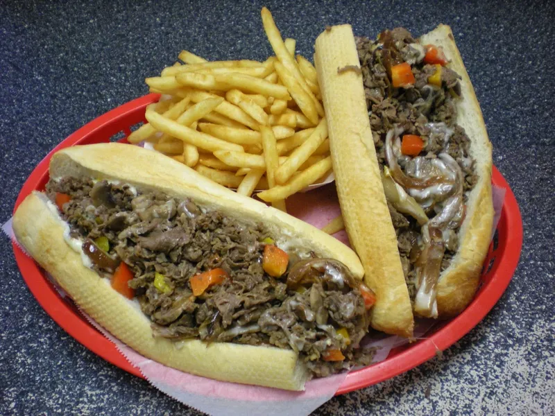 A Philly cheesesteak hoagie with fries in a red basket at Phillys Cafe & Deli