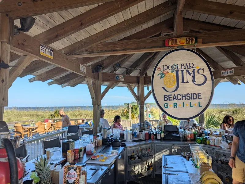 The thatched-roof tiki bar at Pool Bar Jim's with the Pool Bar Jim's Beachside Grill sign and the beach beyond