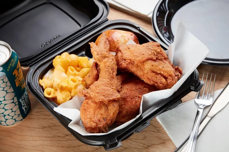 Fried chicken and macaroni and cheese with a roll in an open black takeout container