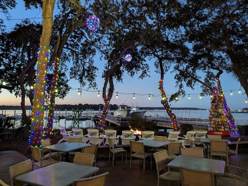 The lit patio at Skull Creek Boathouse at dusk, with tables under the trees and the creek and docks beyond