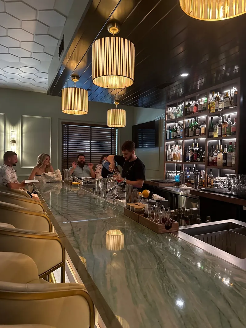 The long stone bar at Starbird Spirits & Bites, with bartenders at work, pendant lights and a wall of bottles
