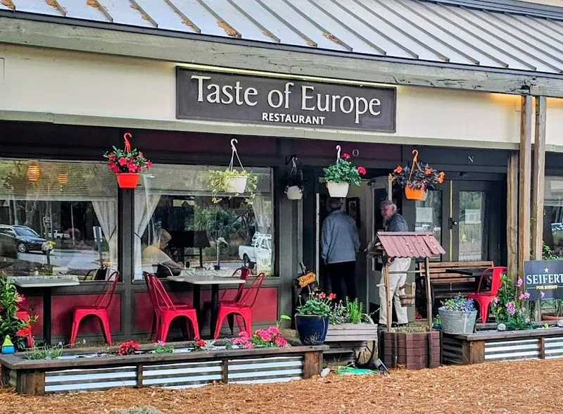 The front of Taste of Europe restaurant with its sign, red chairs and flower boxes along the patio
