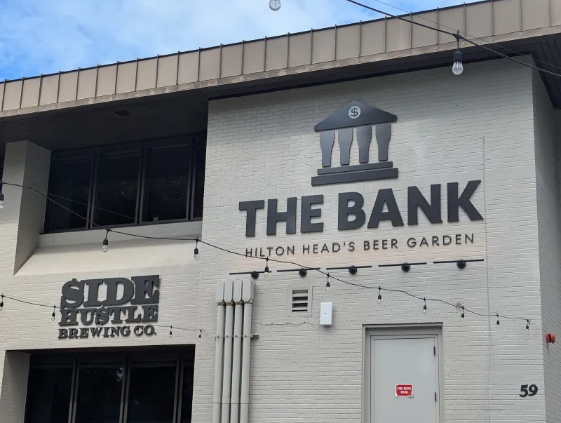 The Bank’s brick front at 59 Pope Avenue, with its sign reading Hilton Head’s Beer Garden and the Side Hustle Brewing Co. sign beside it