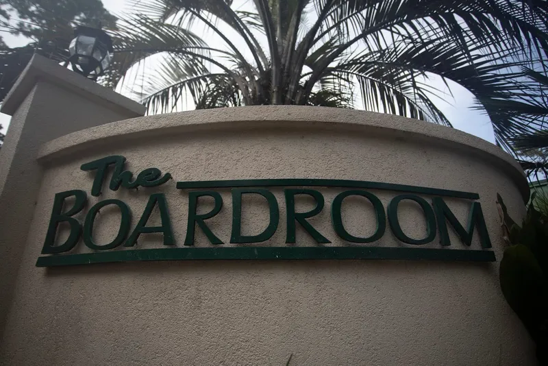 The Boardroom sign on a curved stucco wall with palm fronds behind it