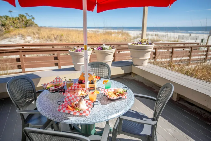 A table under a red umbrella on The Dunes House deck, with the dunes and ocean behind