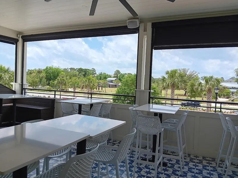 The upstairs dining room at The Lobster Bar, with white tables beside open windows that look out over palm trees