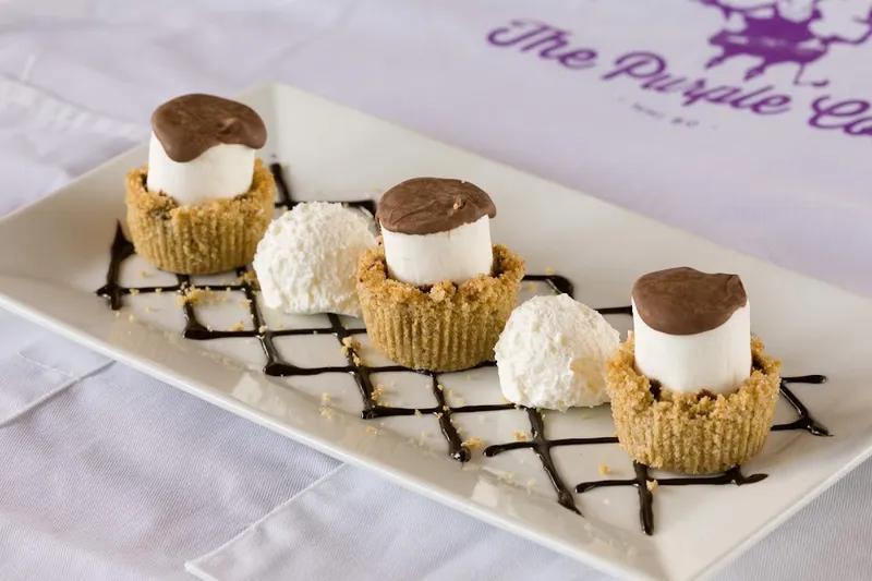Three marshmallow-topped mini cheesecakes on a white plate printed with the Purple Cow logo