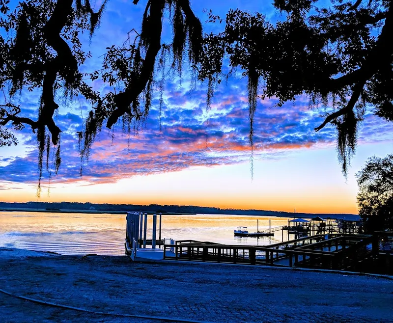 A pink and orange sunset under live oaks over the May River and docks at Oyster Factory Park in Bluffton
