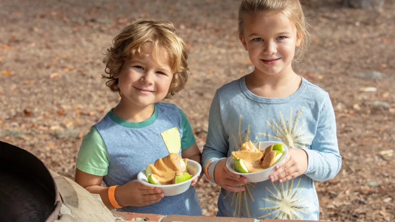Two children holding bowls of apple slices dipped in caramel at the Sea Pines Caramel Apple Festival