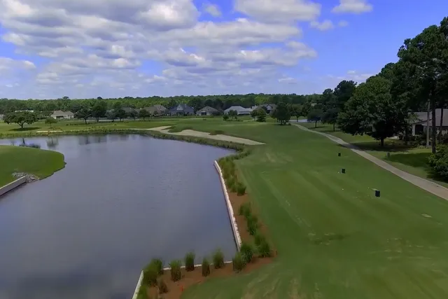 Aerial view down a fairway beside a lagoon toward bunkers at Hampton Hall Club