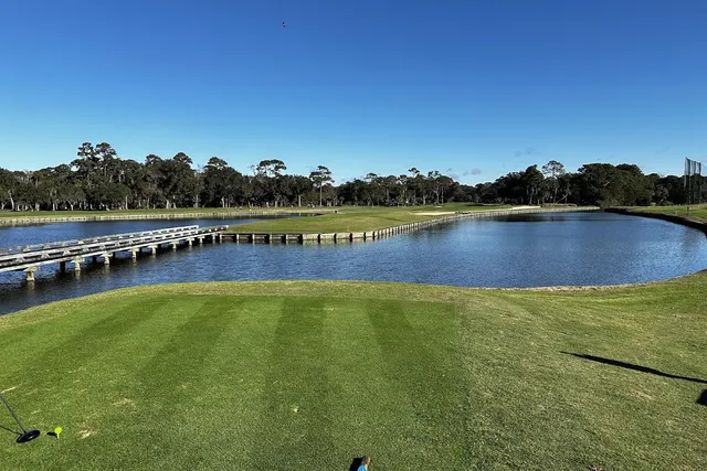 A tee box at Heron Point by Pete Dye looking across a lagoon to the fairway, with a wooden cart bridge on the left