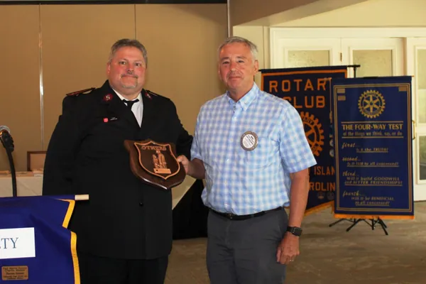 A plaque presentation at a Rotary Club of Hilton Head Island meeting, in front of the club banners